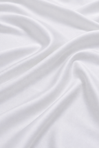 Close-up of silky white bamboo fabric with a soft sateen sheen, premium bamboo bed linen texture.